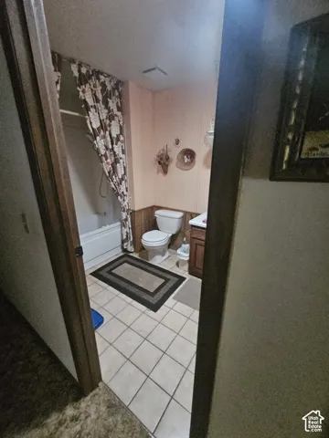 Bathroom featuring a white porcelain toilet, bathtub with a surround, wood-finish cabinetry, and ceramic tile flooring