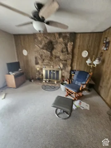 Floor-to-ceiling stone fireplace featuring a metal fire screen, wood-paneled walls, and a ceiling-mounted fan with light fixture