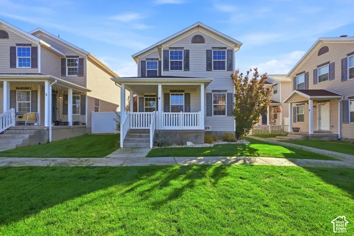 Two-story residence featuring light-colored horizontal siding, dark decorative shutters, a covered front porch with white railing, and a gabled roofline