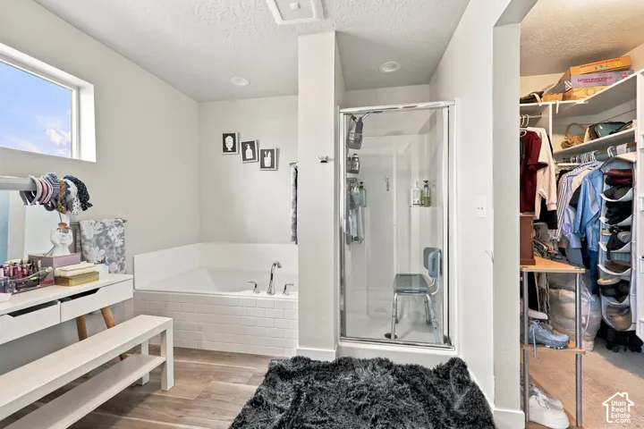 Soaking tub with white tile surround, glass-enclosed shower, wood-finish flooring, recessed lighting, and walk-in closet with built-in shelving