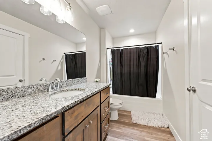Bathroom featuring a wood-finish vanity with a stone-composite countertop, integrated sink, wood-finish flooring, and a shower-tub combination