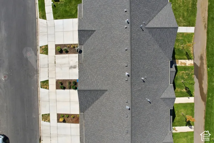 Aerial view of the property featuring a multi-gabled asphalt shingle roof, concrete driveways, and manicured landscaping