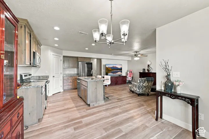 Kitchen featuring wood-finish flooring, a central island with a stone-surface countertop, cabinetry with a natural finish, stainless steel appliances, and a multi-arm chandelier