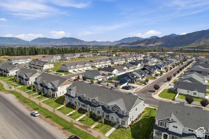 Aerial perspective featuring multi-story residential structures with composite shingle roofing, paved street infrastructure, concrete sidewalks, and a prominent mountain range backdrop