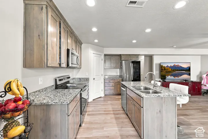 Kitchen featuring light wood-finish cabinetry, stone-patterned countertops, recessed ceiling lighting, wood-finish flooring, and a central island with a double-basin stainless steel sink