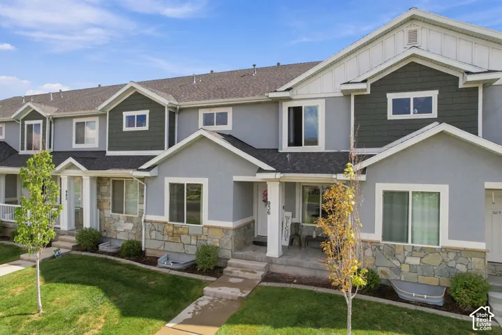 Multi-level exterior featuring grey stucco siding, stone veneer accents, white trim, and shingle roofing