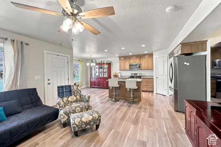 Open-concept kitchen featuring wood cabinetry, stone countertops, a central island with bar seating, and wood-finish flooring throughout
