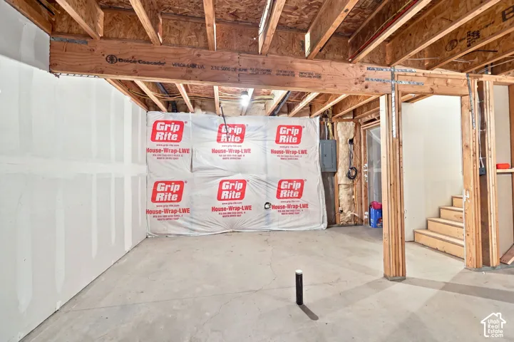 Unfinished space featuring exposed timber framing, concrete flooring, exterior moisture barrier wall covering, and a structural engineered wood beam
