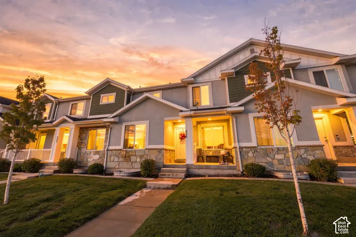 Multi-family exterior featuring light-colored stucco and natural stone veneer, dark green vertical siding accents, gabled rooflines, and concrete walkways