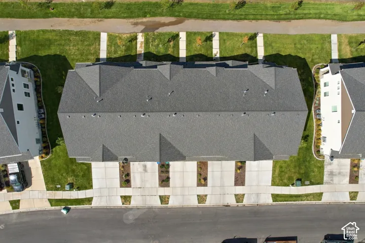 Aerial view featuring a multi-unit property with a composite shingle roof, concrete driveways, and landscaped grass frontage