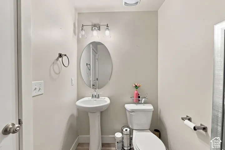 Pedestal sink with a polished chrome faucet, oval wall-mounted mirror, three-light brushed nickel fixture, and matching towel hardware