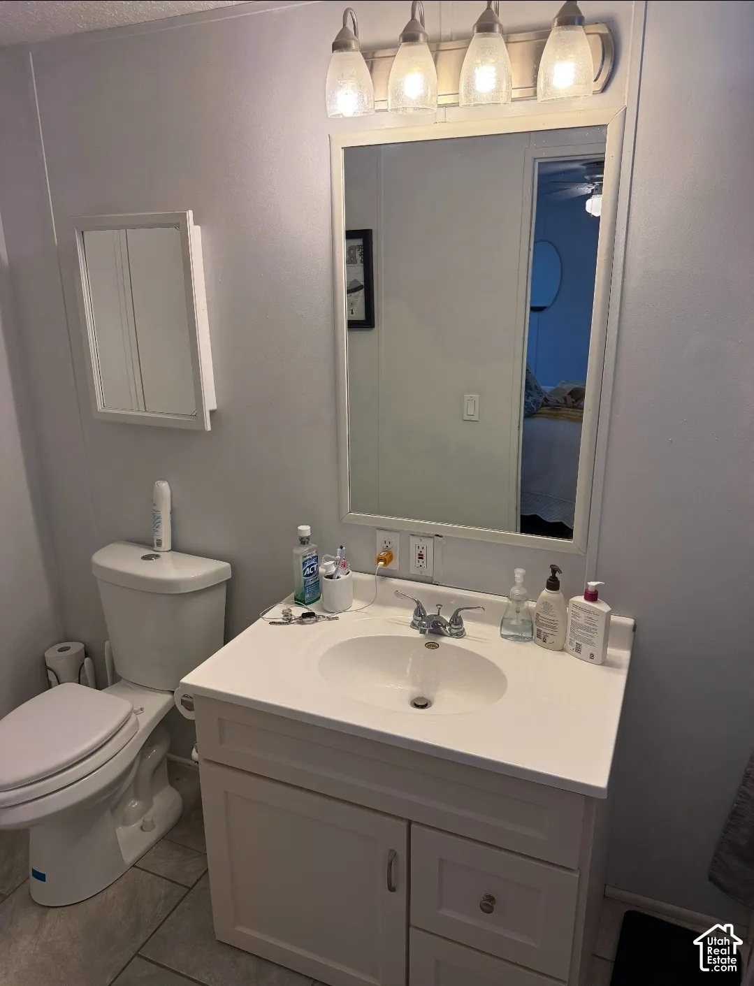 Bathroom featuring a vanity with a white countertop and integrated sink, four-light vanity fixture, framed wall mirror, and wall-mounted storage cabinet