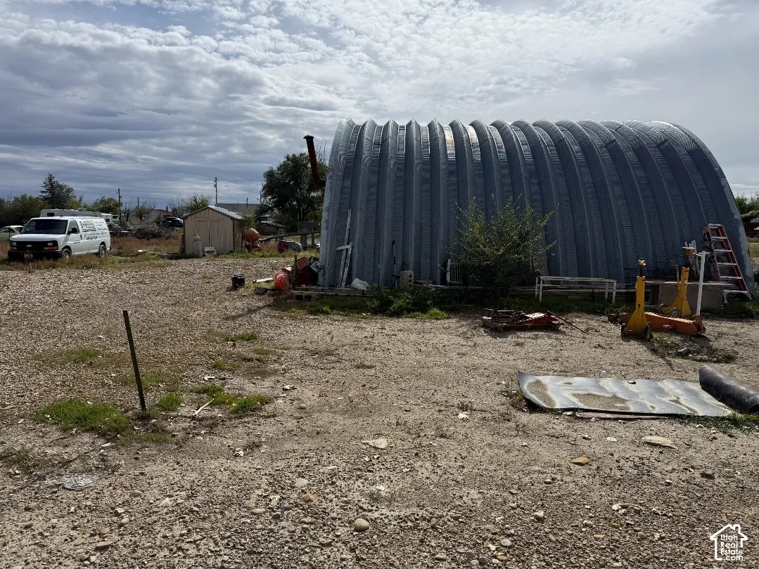 Quonset-style metal outbuilding featuring a corrugated steel exterior, gravel grounds, and an additional storage shed
