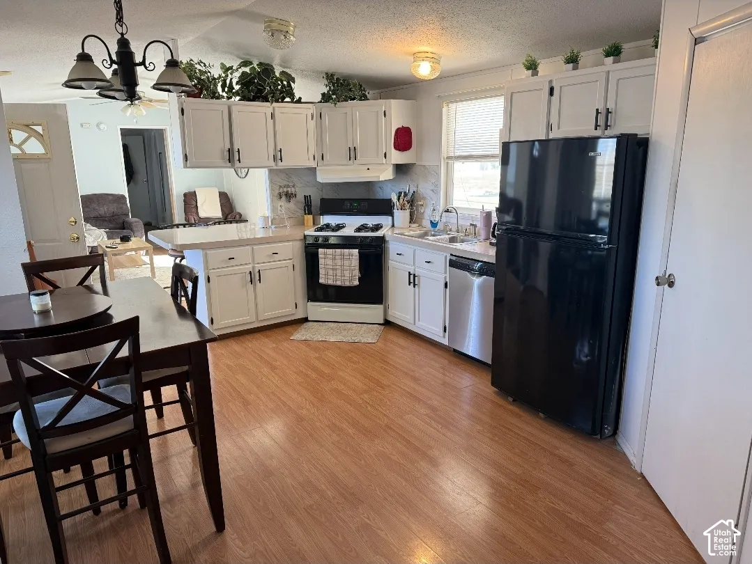 Kitchen featuring white cabinetry, wood-finish flooring, a stainless steel dishwasher, a black freestanding range, and a black refrigerator