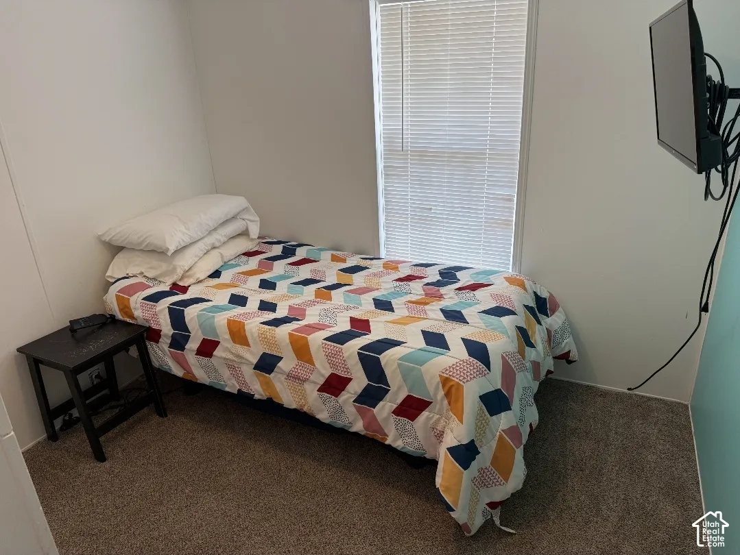 Neutral-toned carpeted flooring and a single window with horizontal blinds