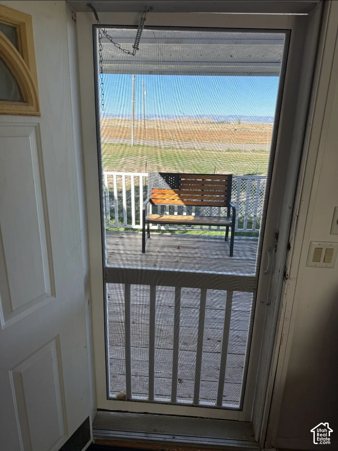 Exterior entry featuring a screen door, wood-decking porch, and white metal railing with expansive open landscape surroundings