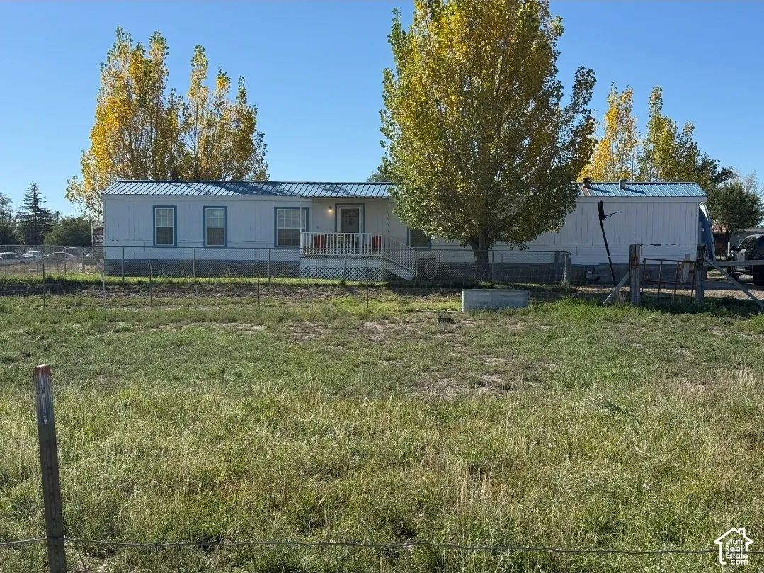 Single-level residence featuring a metal roof, white siding, and a front porch, set on a parcel with chain-link fencing and mature trees