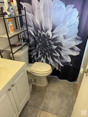 Bathroom featuring a white vanity cabinet with a molded countertop and sink, tile flooring, and a porcelain toilet