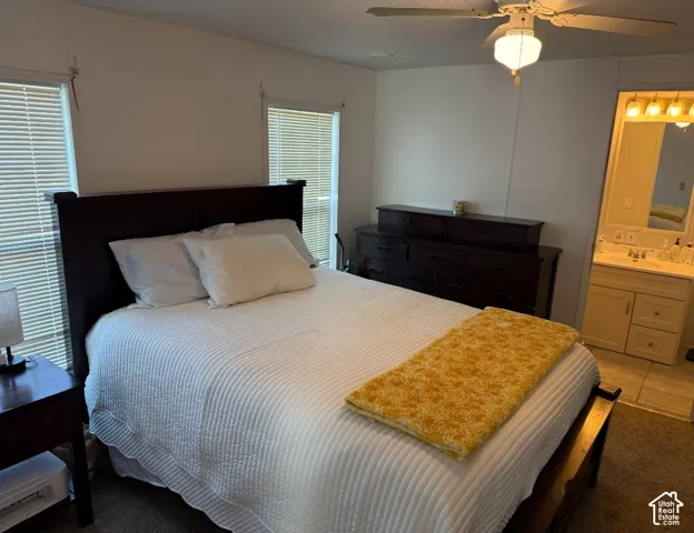 Neutral wall finishes, two windows with horizontal blinds, ceiling fan with integrated lighting, and vanity with stone-style countertop