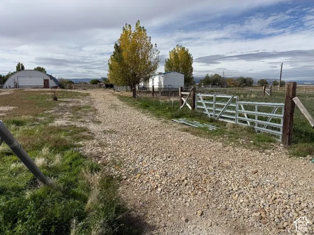 Gravel driveway leading to expansive grounds, metal arched outbuilding, perimeter wire fencing, and industrial-style metal gate