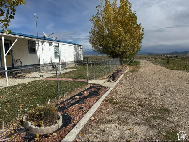 Exterior featuring white metal siding, a blue metal roof, chain-link perimeter fencing, and a gravel driveway