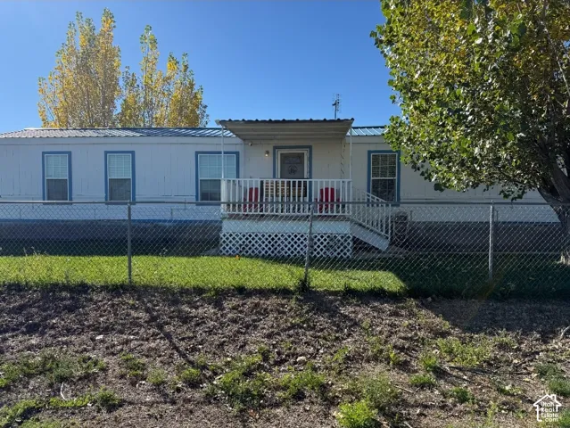Exterior featuring a metal roof, white siding, covered front porch with white railing, lattice skirting, and chain-link fencing