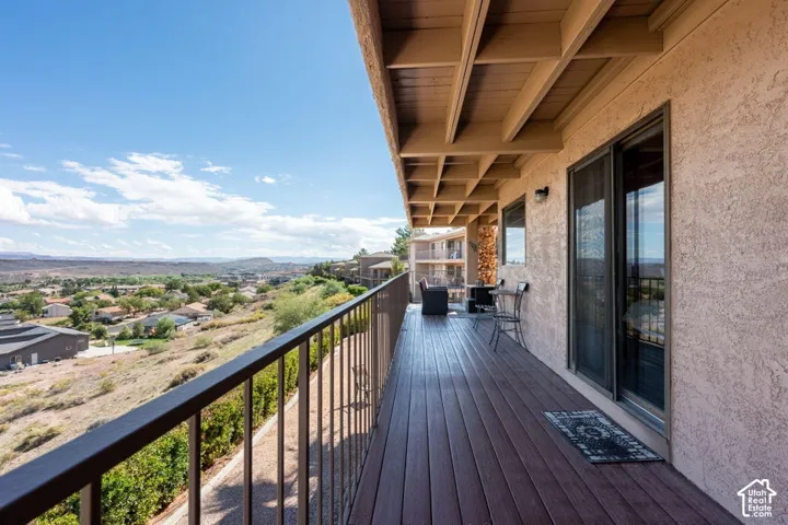 Covered deck featuring wood-finish decking, exposed beam ceiling, metal railing, and sliding glass doors