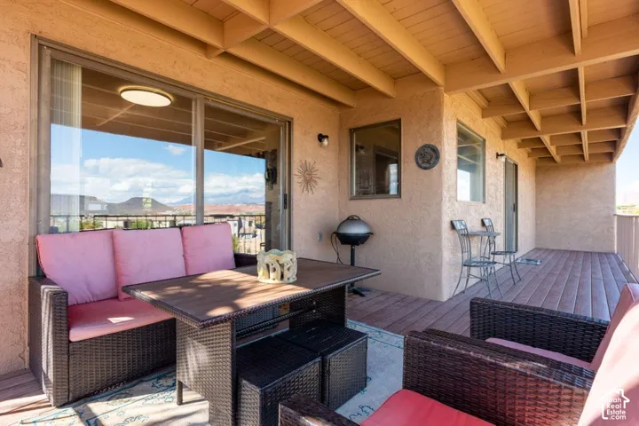 Covered balcony featuring wood-finish decking, an exposed beam ceiling, sliding glass doors, and mountain backdrop