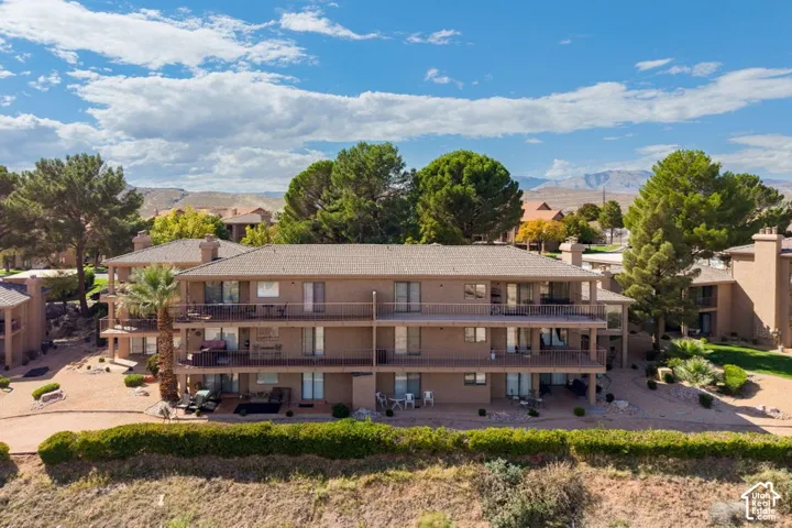 Multi-level structure featuring a hipped roof, beige stucco exterior, tiered metal balconies, and mature palm and coniferous landscaping