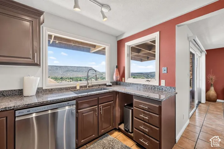 Kitchen featuring dark wood cabinetry, stone-finish countertops, stainless steel dishwasher, tile flooring, and windows with mountain scenery