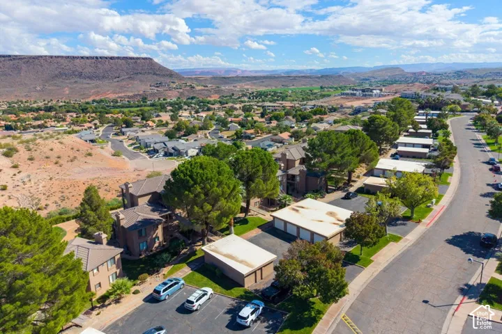 Aerial perspective featuring multi-level residential structures, designated parking areas, detached garage buildings, mature landscaping, and an expansive mountain backdrop