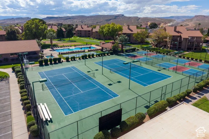 Multiple hard-surface tennis courts enclosed by chain-link fencing, featuring exterior lighting and mountain scenery