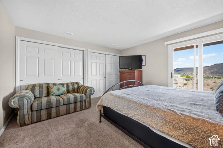 Neutral wall color, wall-to-wall carpeting, dual sets of white paneled sliding closet doors, and sliding glass doors with access to an exterior deck featuring a mountain backdrop