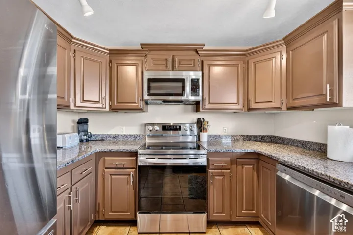Kitchen featuring raised-panel wood cabinetry, stone-patterned countertops, stainless steel appliances, and tile flooring