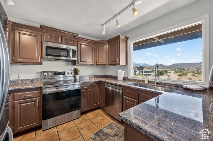 Kitchen featuring stained wood cabinetry, stone-finish countertops, stainless steel appliances, ceramic tile flooring, and a window with mountain scenery