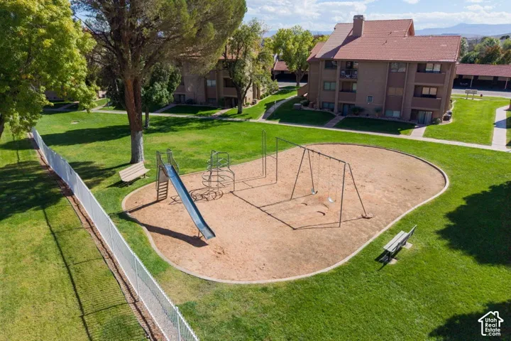 Community recreational area featuring a metal slide, climbing structure, swing set, and two benches situated on a manicured lawn
