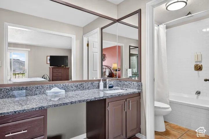Bathroom vanity featuring a speckled stone countertop, dark wood-finish cabinetry with brushed metal hardware, a full-width wall mirror, and a tile-surround bathtub