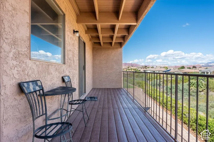 Covered balcony featuring wood-finish flooring, stucco exterior walls, an exposed beam ceiling, and a metal railing