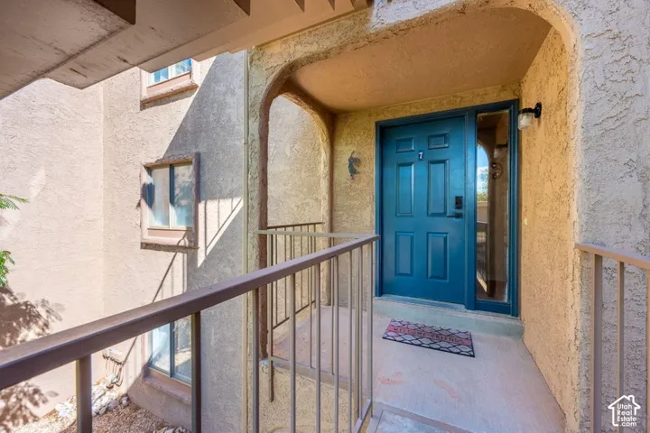 Covered entry porch featuring stucco walls, a recessed arched entryway, metal railing, and a paneled door with sidelight