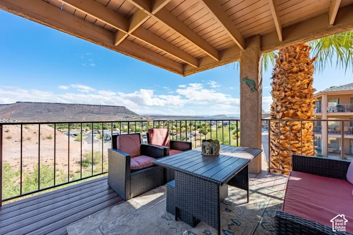 Covered balcony featuring wood-finish decking, exposed beam ceiling, metal railing, and mountain backdrop