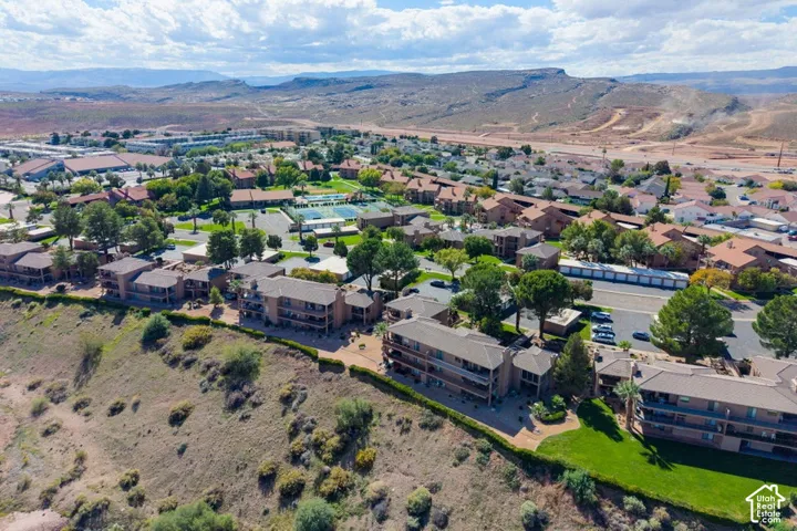 Aerial perspective of a multi-level residential complex featuring terracotta-toned exterior siding, expansive balcony structures, manicured lawn areas, and an elevated hillside location with mountain backdrops