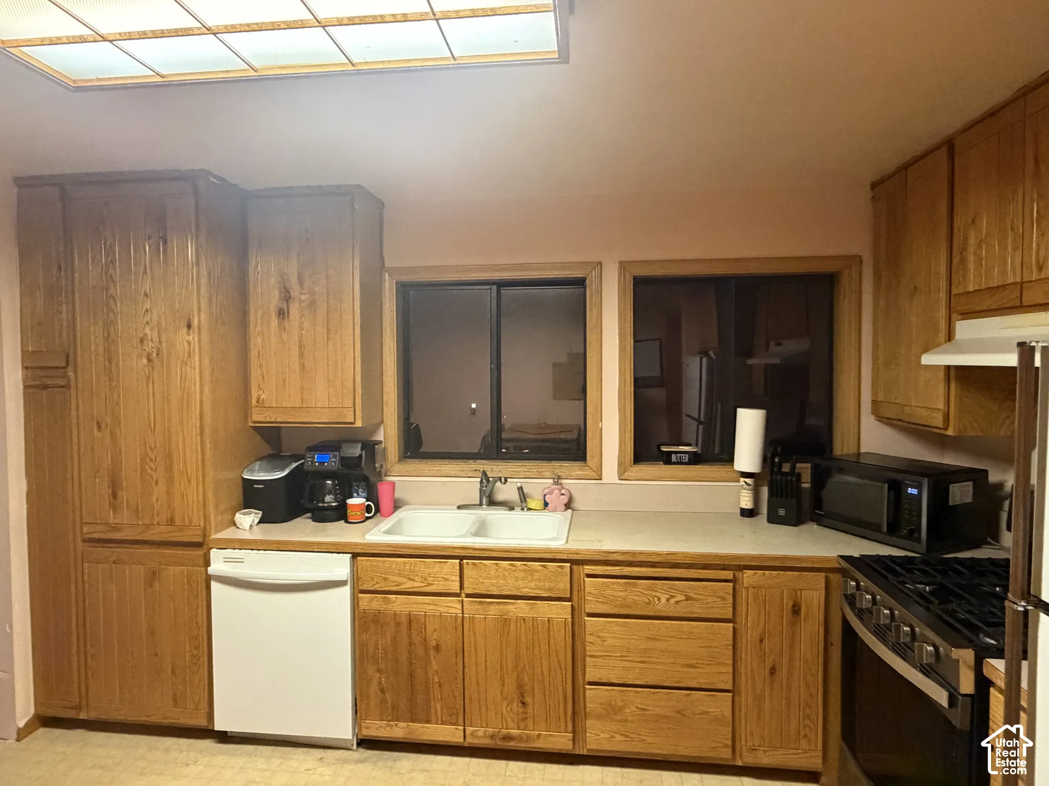 Kitchen featuring wood cabinetry, solid-surface countertops, double-basin sink, integrated dishwasher, and recessed ceiling lighting