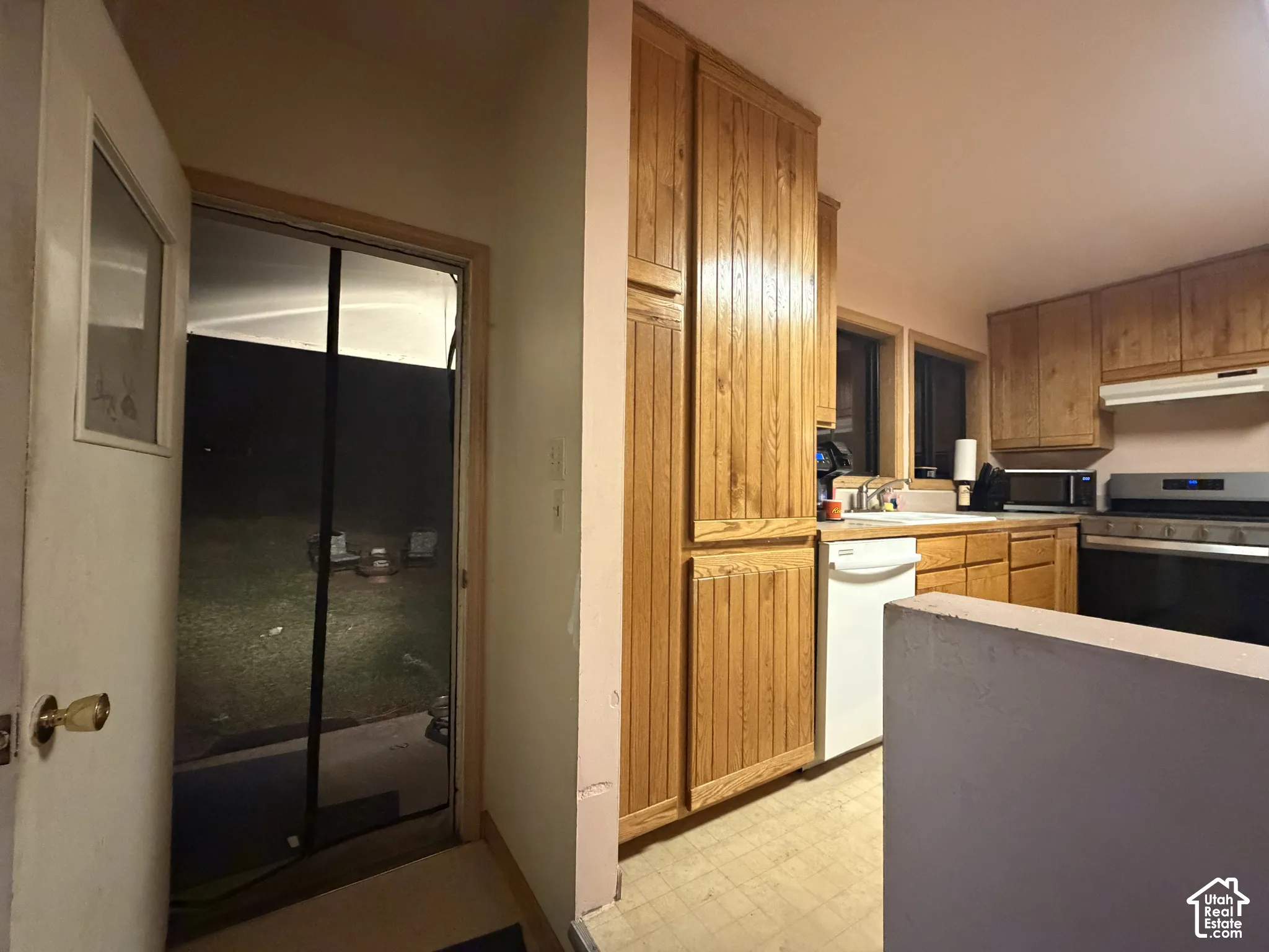 Kitchen featuring light-finish wood cabinetry, floor-to-ceiling pantry storage, neutral floor tiling, and white appliances