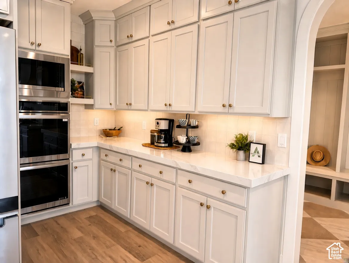 Kitchen featuring floor-to-ceiling Shaker-style cabinetry, white countertops, built-in double wall ovens, wood-finish flooring, and recessed under-cabinet lighting