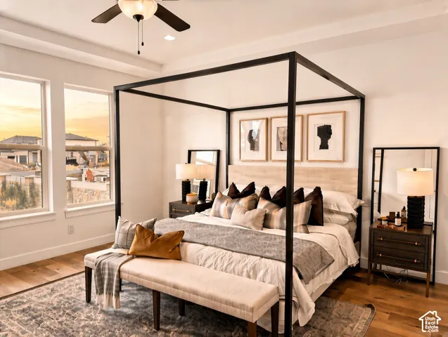 Bedroom featuring wood-finish flooring, recessed tray ceiling, ceiling fan with integrated lighting, and expansive windows