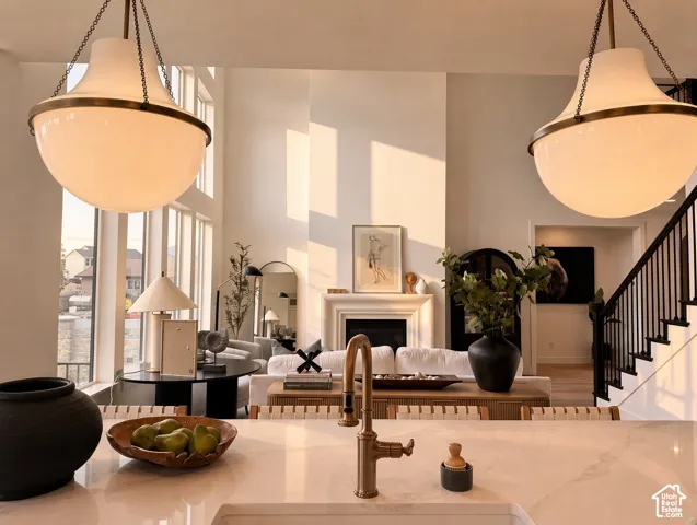 Kitchen featuring a solid-surface island with a bridge-style faucet and dual bell-shaped pendant lights, floor-to-ceiling windows, and a fireplace with a decorative mantel