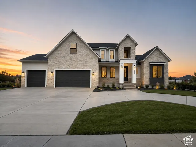 Custom stone veneer exterior with dual-car and single-car garage bays, steep-pitched rooflines, expansive concrete driveway, and covered entryway