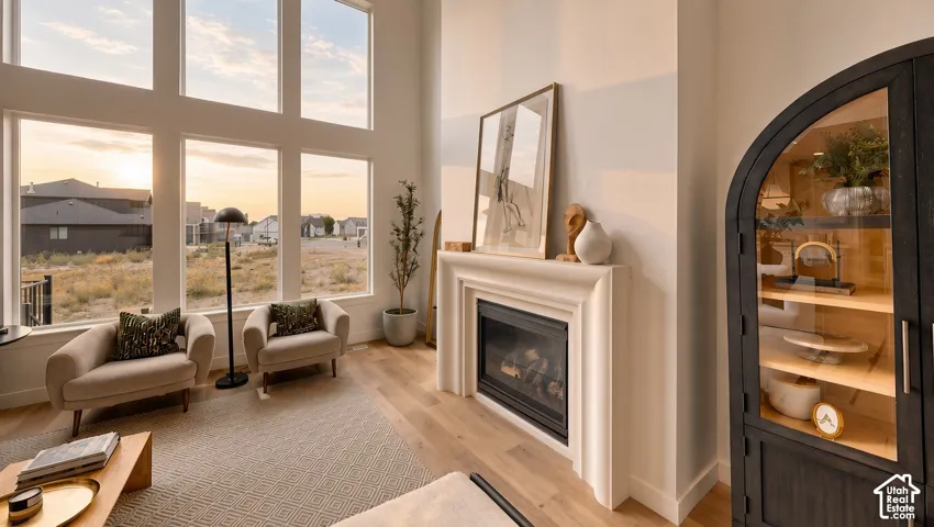 Floor-to-ceiling windows, soaring ceilings, gas fireplace with a decorative stone surround, and wood-finish flooring