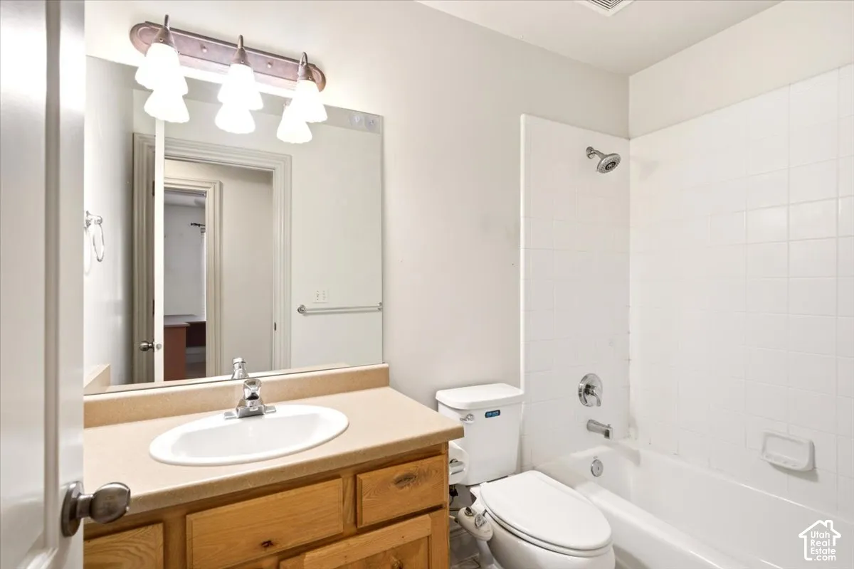 Bathroom featuring a vanity with a neutral-toned countertop and an integrated oval sink, a wall-mounted light fixture with frosted glass shades, a wall-to-wall mirror, and a porcelain tub with a tiled surround