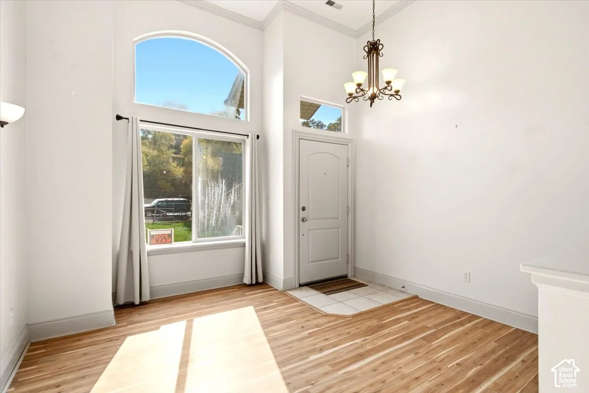 Foyer featuring soaring ceilings, wood-finish flooring, an arched transom window, ceramic tile entryway, and decorative chandelier